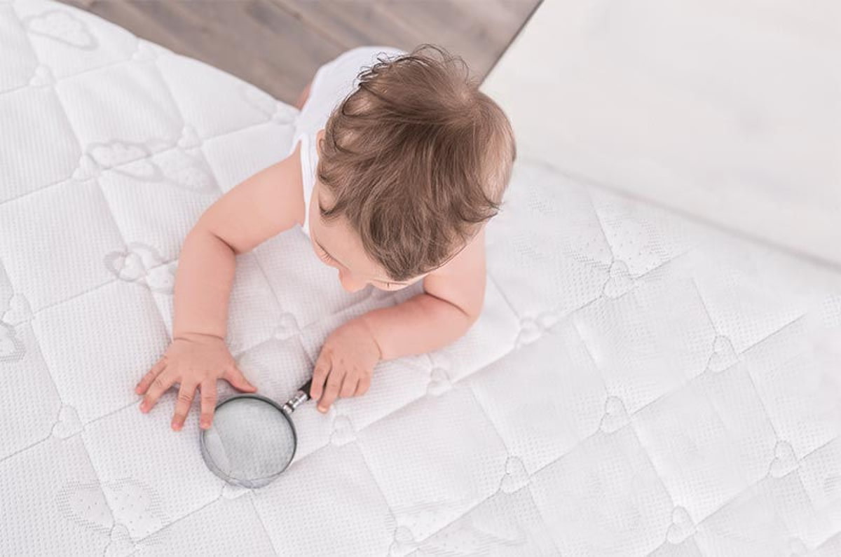 Niño con lupa encima de una funda de colchón Träumeland