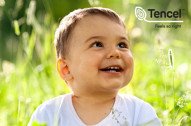 Bebé sentado en la hierba con logotipo TENCEL Bebé sentado en la hierba con logotipo TENCEL