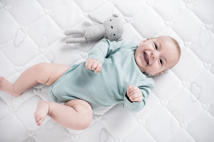 Baby im türkisen Body auf Matratze mit Kuscheltier Baby im türkisen Body auf Matratze mit Kuscheltier
