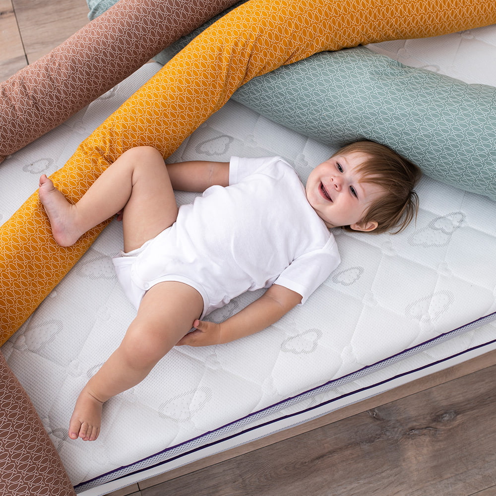 Child lying between the Träumeland snake bed bumpers XL in fish design