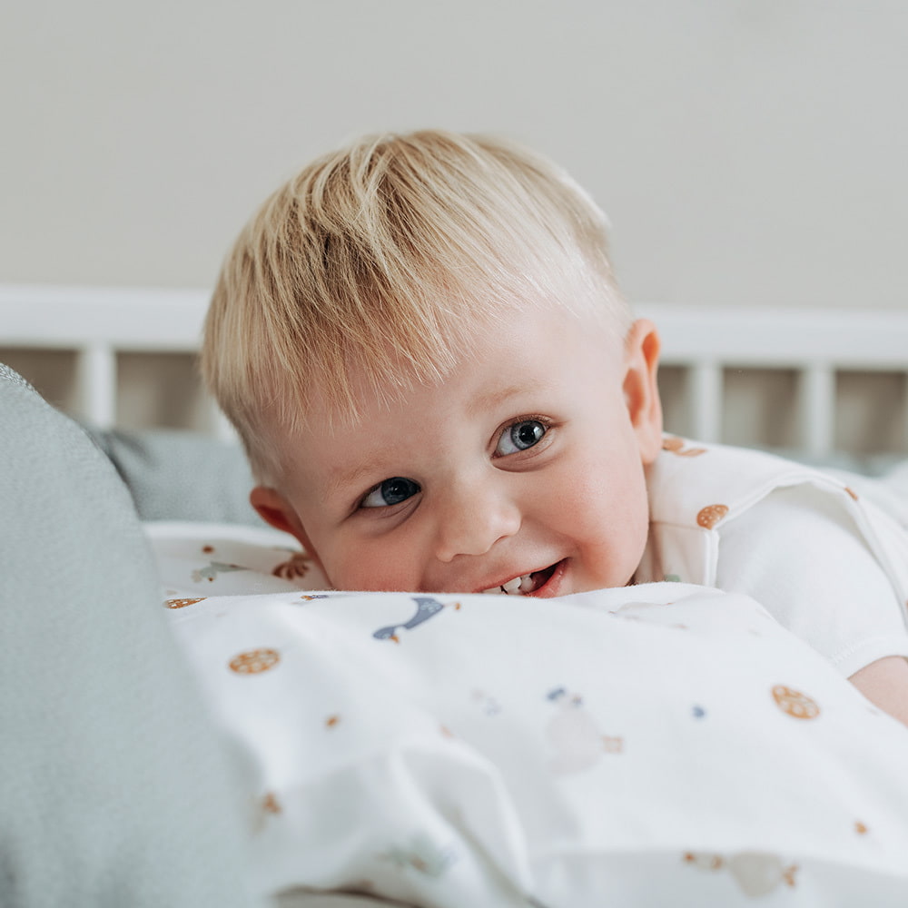 Kind im Bett liegend mit Bettwäsche Kikeriki
