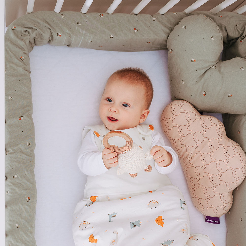 Baby in crib with bed snake and cuddly pillow