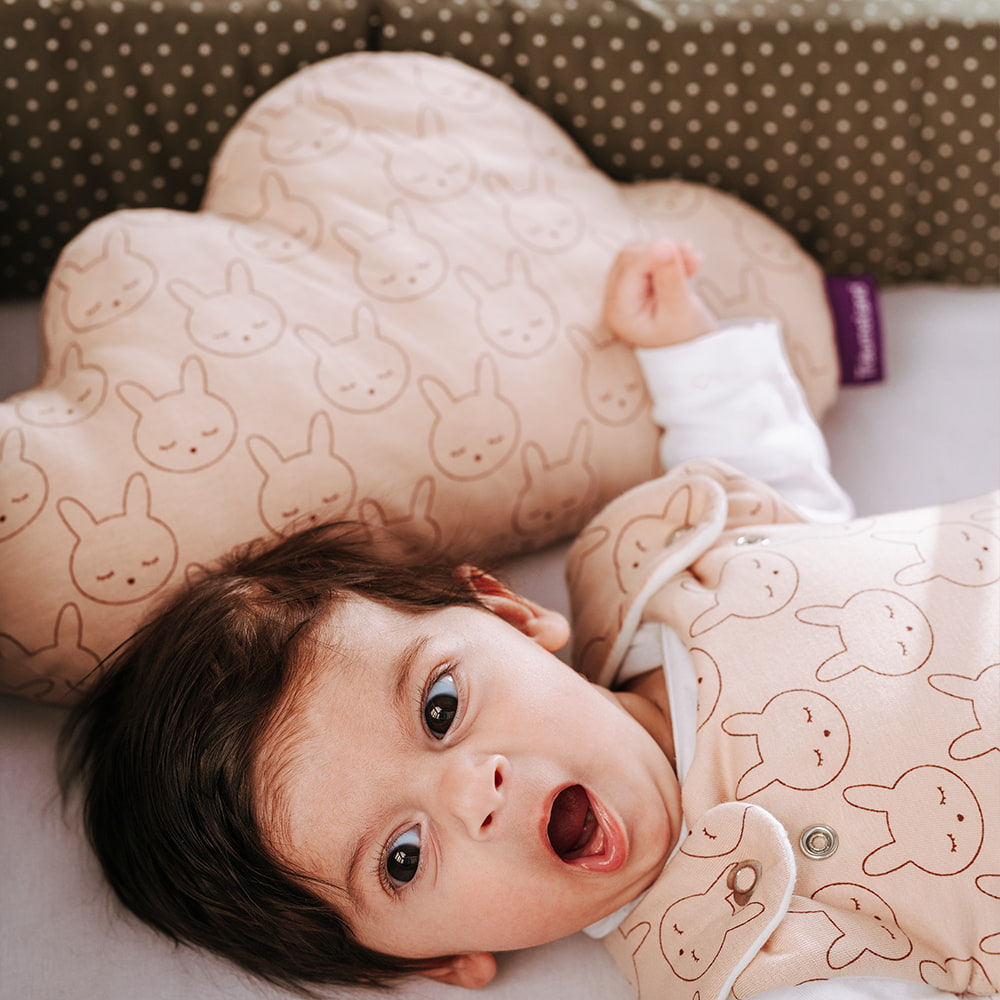 Baby yawning in crib with cuddly pillow