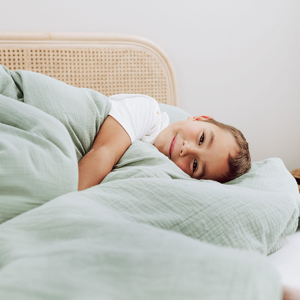 Child in a large bed with cotton muslin bed linen