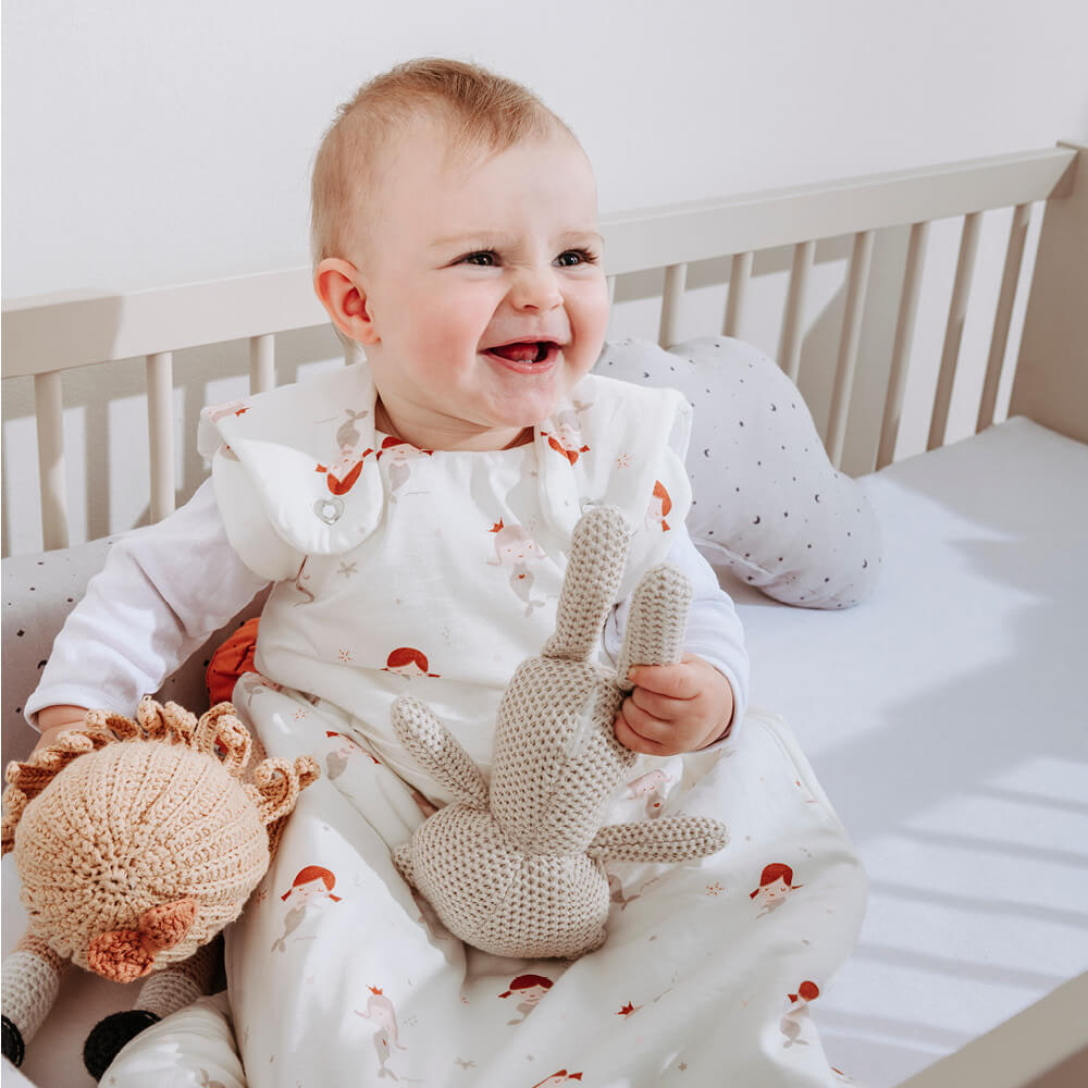 Baby in sleeping bag sitting in crib